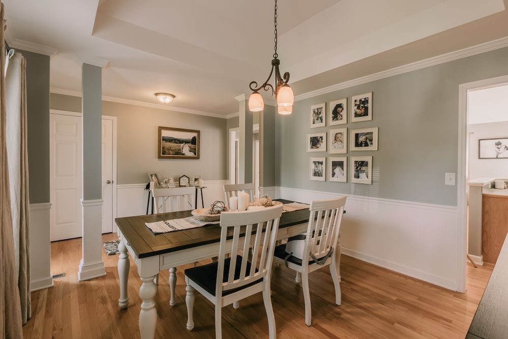 Bright dining area with farmhouse table, white chairs, and gallery wall in sage green room.