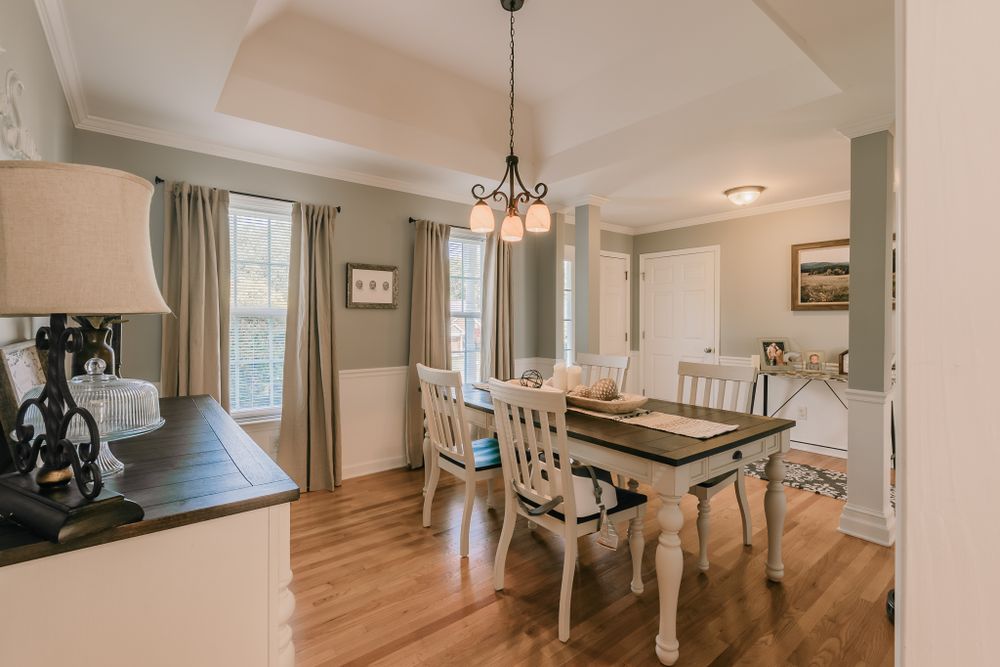 Traditional dining room with chandelier, wooden table and white chairs on hardwood floors.