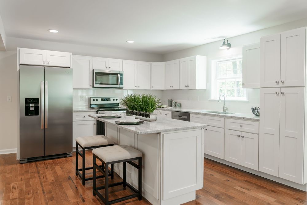 Modern white kitchen with stainless steel appliances, island with bar stools, and hardwood flooring.
