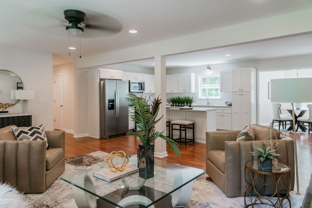 Open concept living room and kitchen with brown leather chairs and glass coffee table.