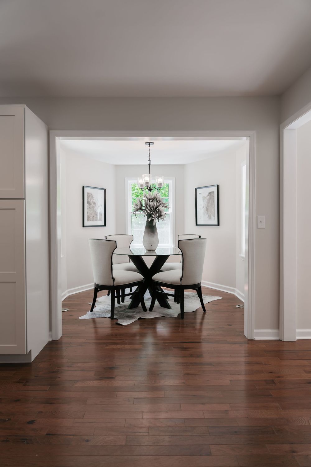 Elegant dining nook with round black table, white chairs and framed artwork beside a window.