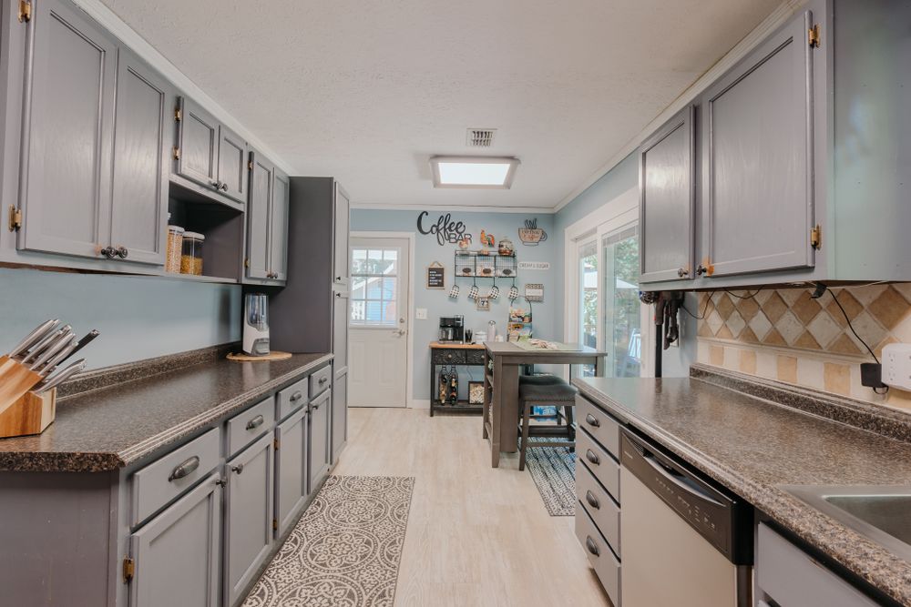 Long galley kitchen with grey cabinets, granite counters, and patterned runner rug.