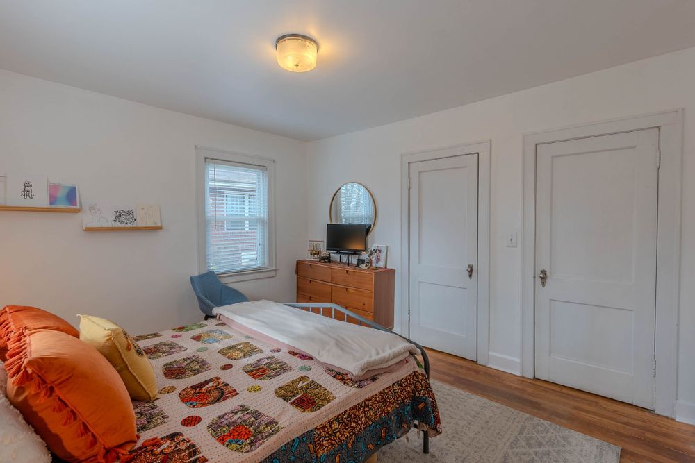 Bright bedroom with patterned bedding, hardwood floors, and round mirror.