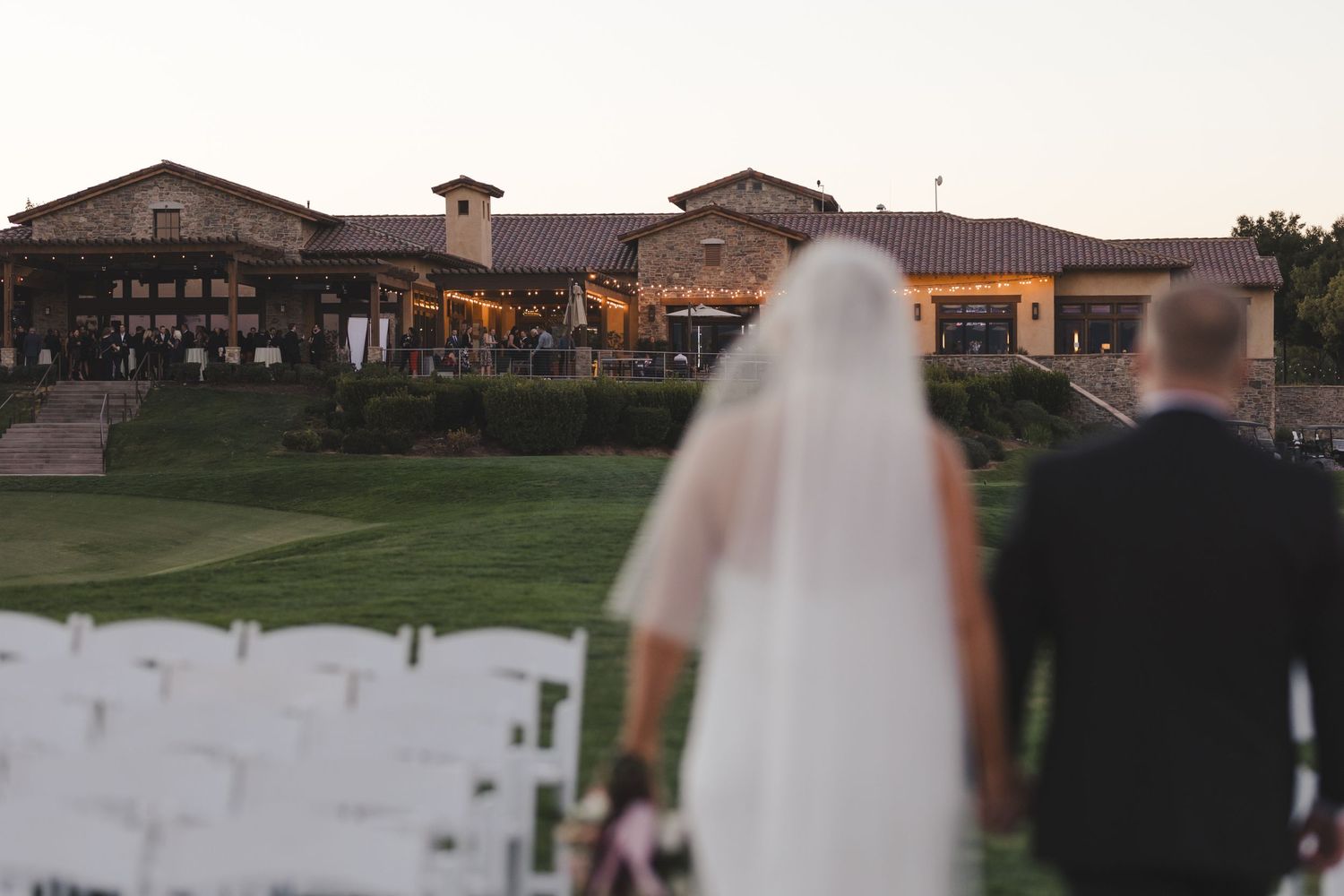 Silhouetted figures on a golf course at sunset with Spanish-style clubhouse buildings in the background.