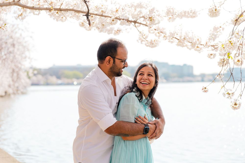 A romantic springtime photo session under blooming cherry blossom trees near a waterfront.