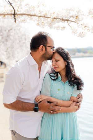 A couple embraces lovingly under cherry blossom trees during a springtime photo shoot.