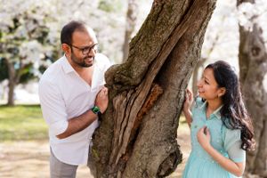 A playful couple poses near cherry blossom trees during a spring photography session.