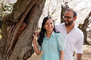 Two people share intimate moments under pink cherry blossom trees during a photo session.