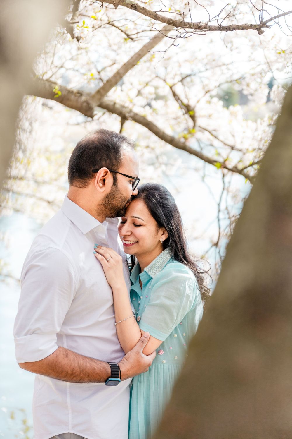 A romantic couple embraces under blooming cherry blossom trees during a spring photo session.