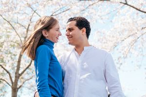 A couple shares joyful moments beneath blooming cherry trees in bright sunlight.