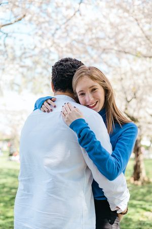 Candid moments of affection captured under cherry blossoms in a park setting.