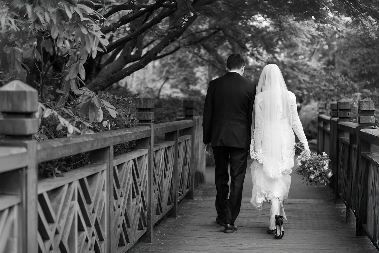 Black and white photo of newlyweds helping each other across rocks by a stream.