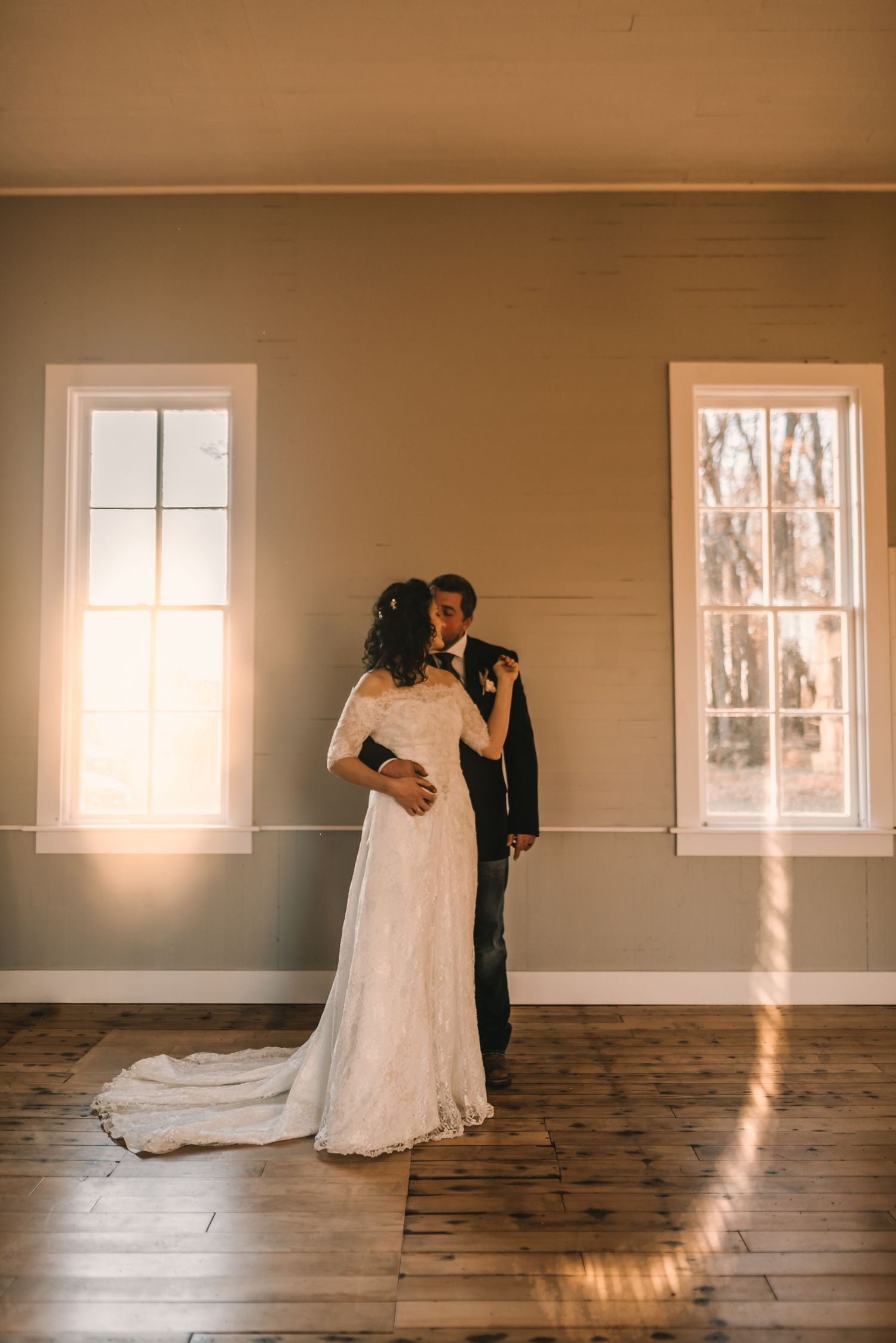 Romantic wedding portrait of couple in minimalist room with sunlit windows.