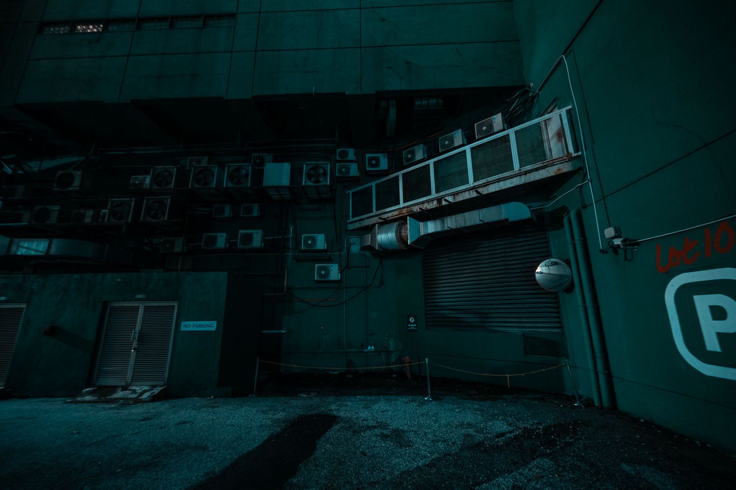 Dark industrial alleyway at night with mounted ladder and graffiti on walls illuminated in eerie teal lighting.
