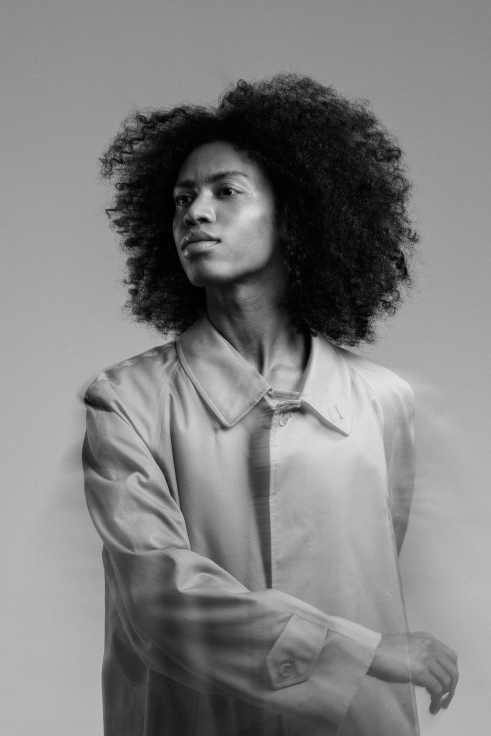 Black and white portrait of figure with striking curly afro hair wearing light colored button-up shirt.