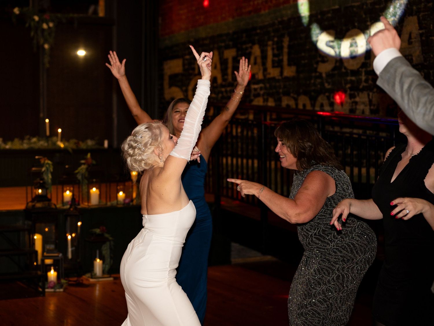 People dancing and celebrating with raised arms on a dark dance floor at a party or wedding reception.