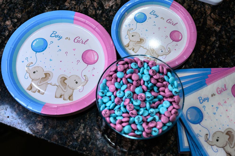 Pink and blue baby shower party plates and matching candy displayed on a dark granite surface.