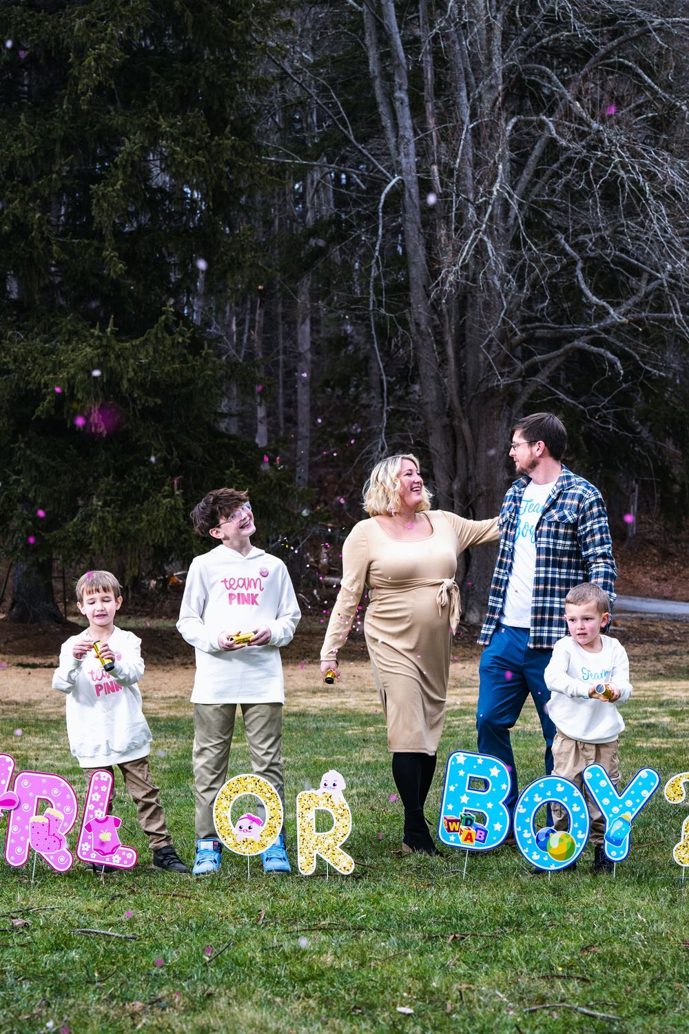 A gender reveal party setup outdoors with colorful letters spelling 'GIRL OR BOY' displayed on grass with people standing behind.
