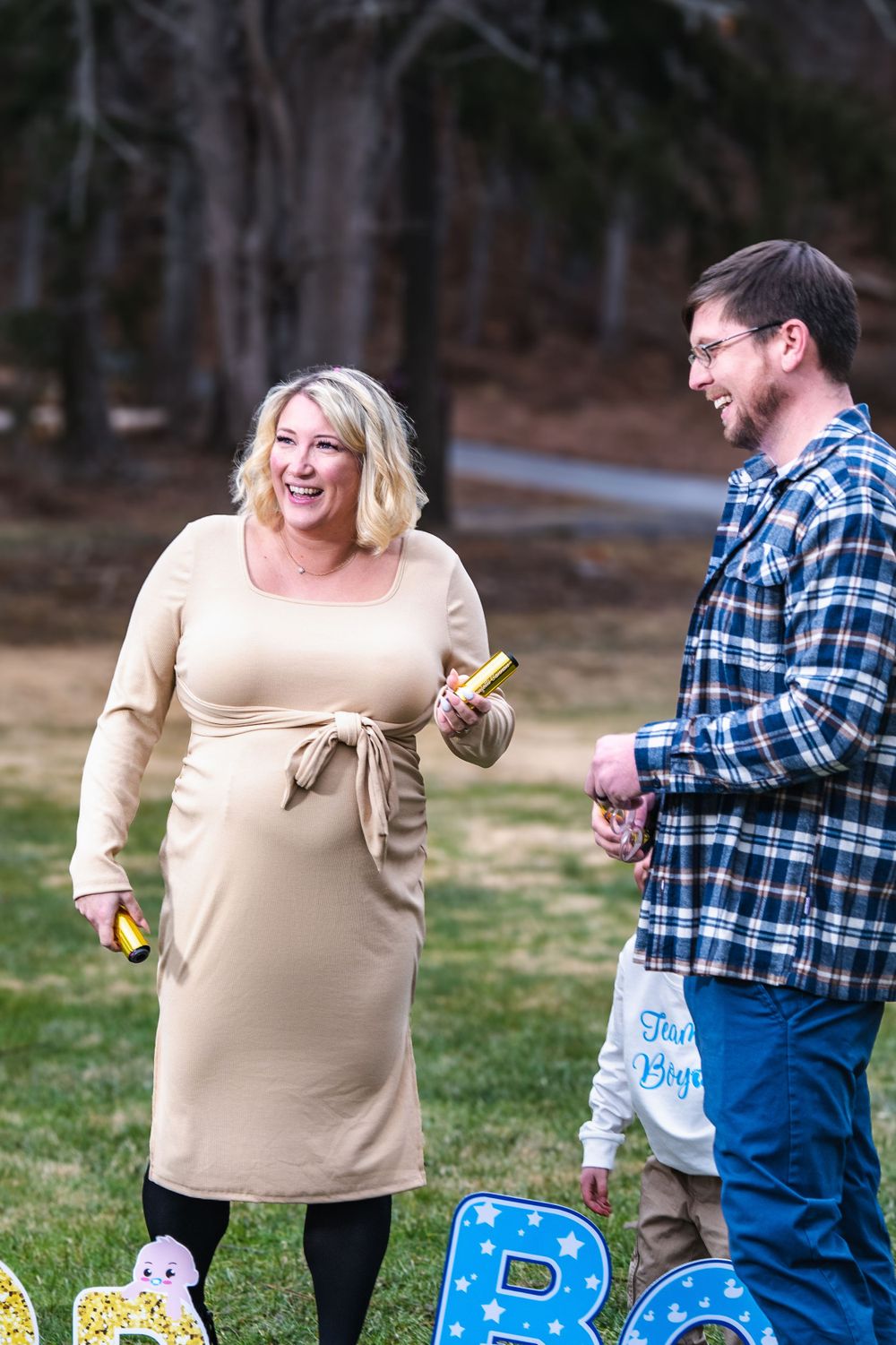 A couple shares a joyful moment outdoors during what appears to be a gender reveal celebration with decorative letters visible.