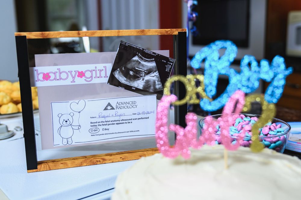 A framed ultrasound photo sits beside a baby shower cake decorated with colorful 'BABY' lettering.