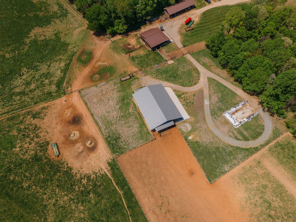 Aerial view of rural buildings and dirt paths surrounded by green forest.