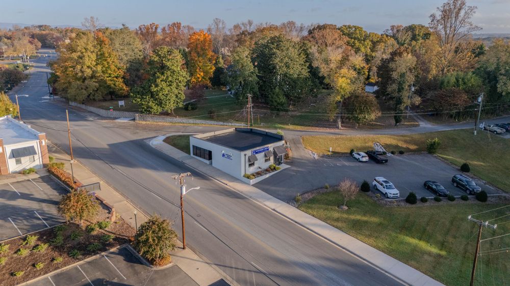 Small white guard booth at an entrance with parking lot and autumn trees in background.