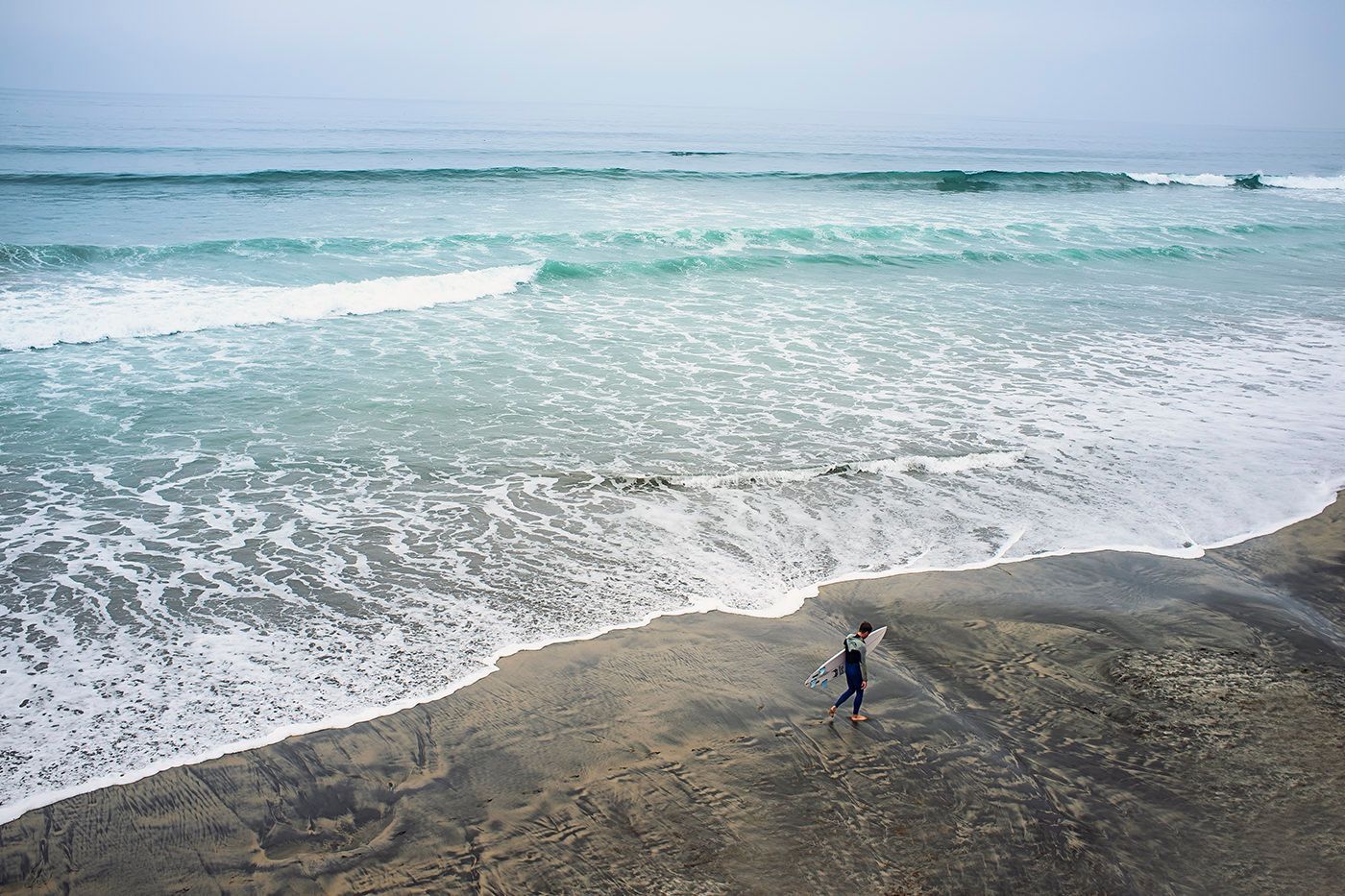 Person standing on rocky outcrop watching waves crash on Australian beach.