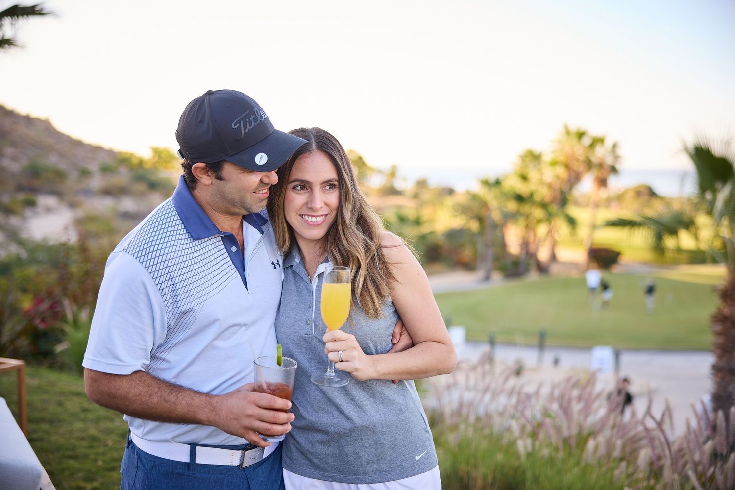Couple enjoying drinks together on a golf course during sunset.