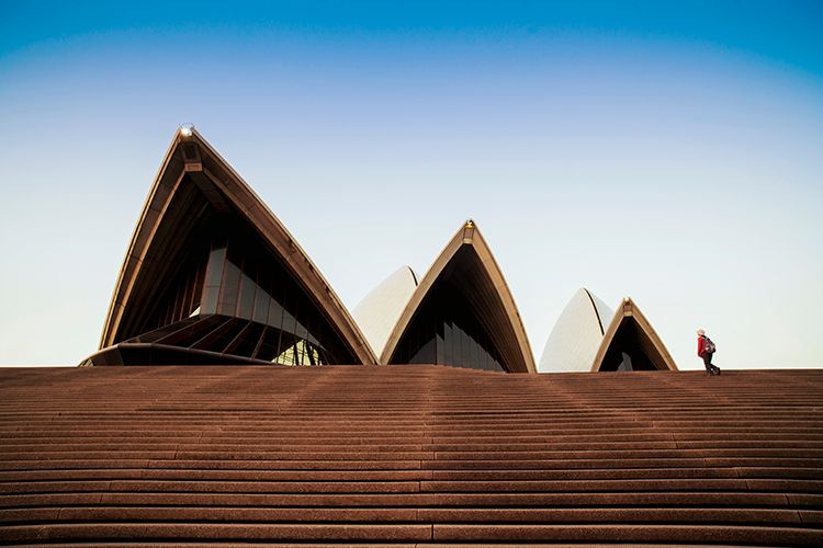 Iconic Sydney Opera House sails against blue sky with dramatic brown steps leading up to the entrance.