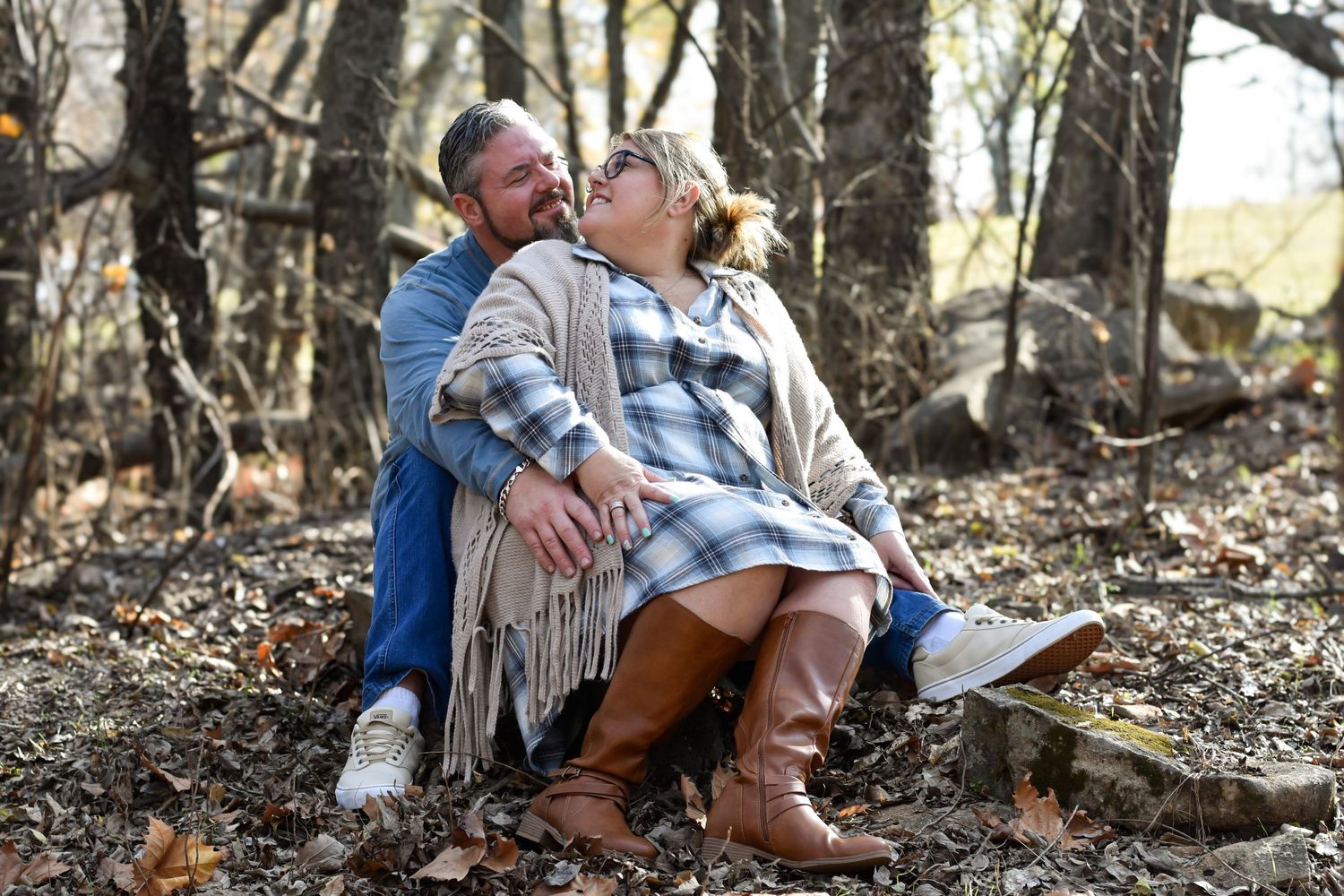A couple seated on the ground in a serene, wooded area, immersed in nature and each other's company.