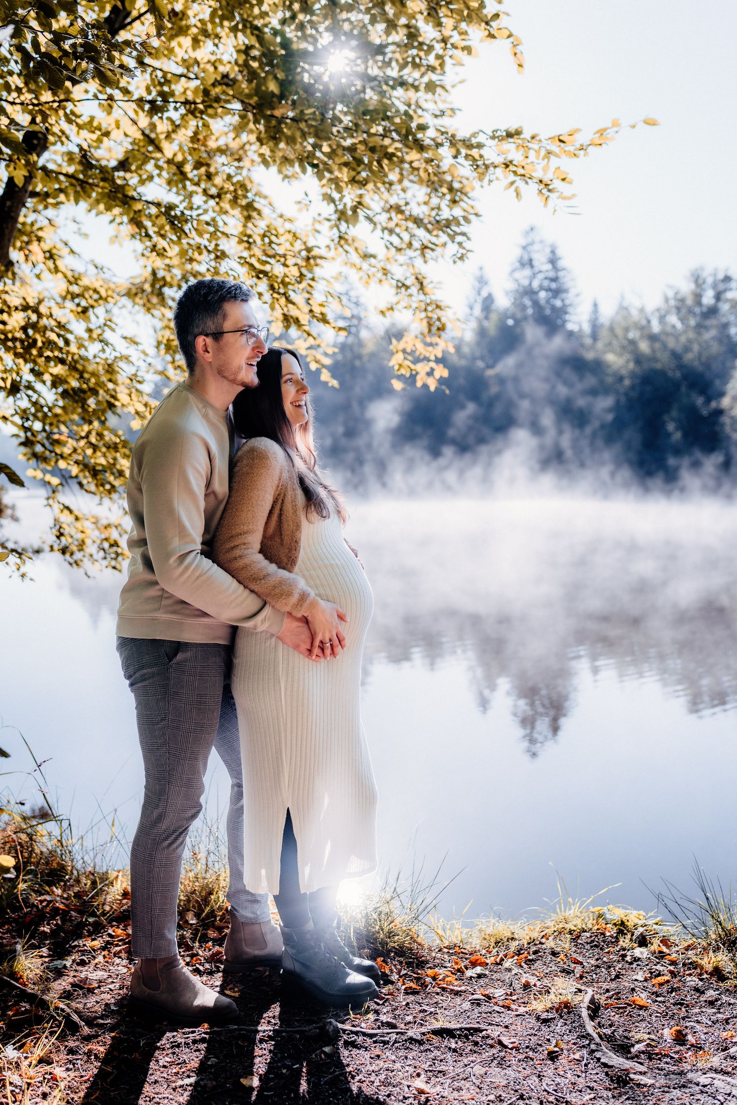 A couple shares an intimate moment by a misty lake during golden hour.