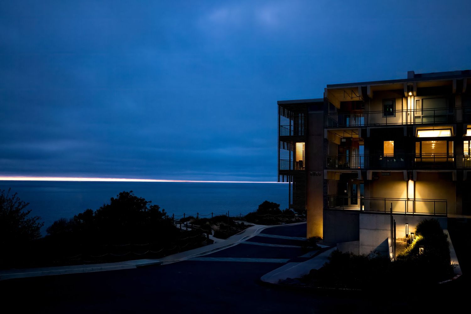 Illuminated coastal building at dusk with light trails and moody blue sky in La Jolla, California.