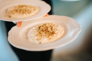 Server carrying two white plates of creamy risotto topped with toasted breadcrumbs at an upscale restaurant.