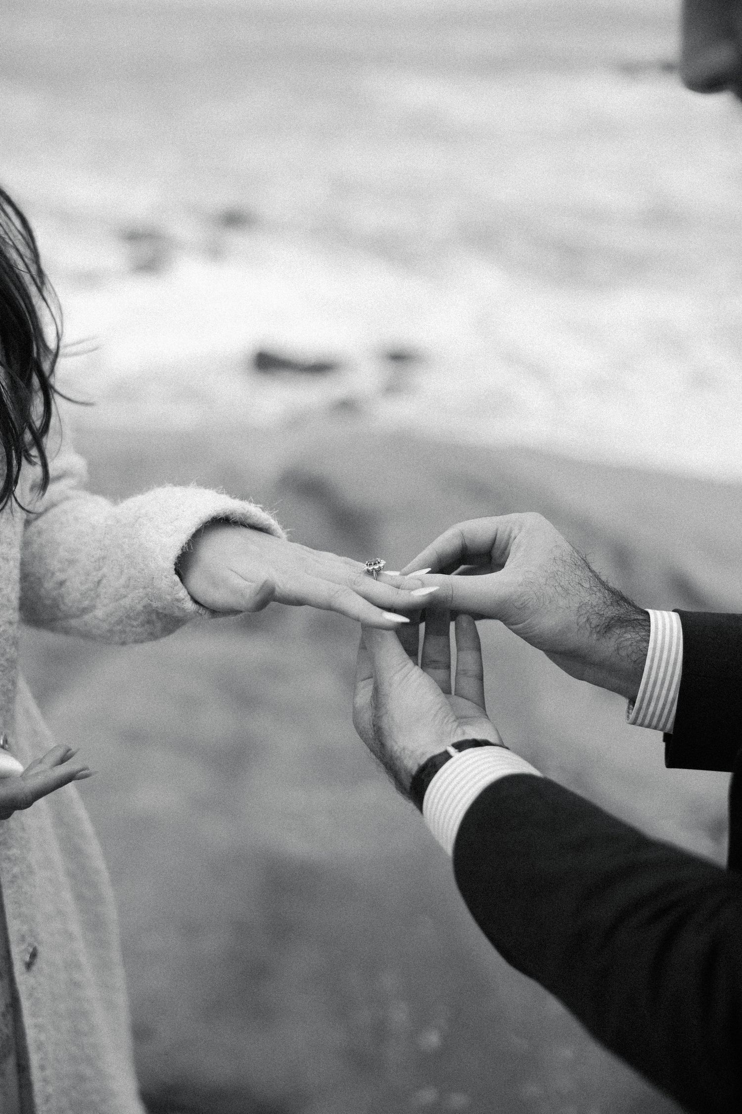 Black and white romantic photo of hands exchanging a ring in a proposal moment by the beach.
