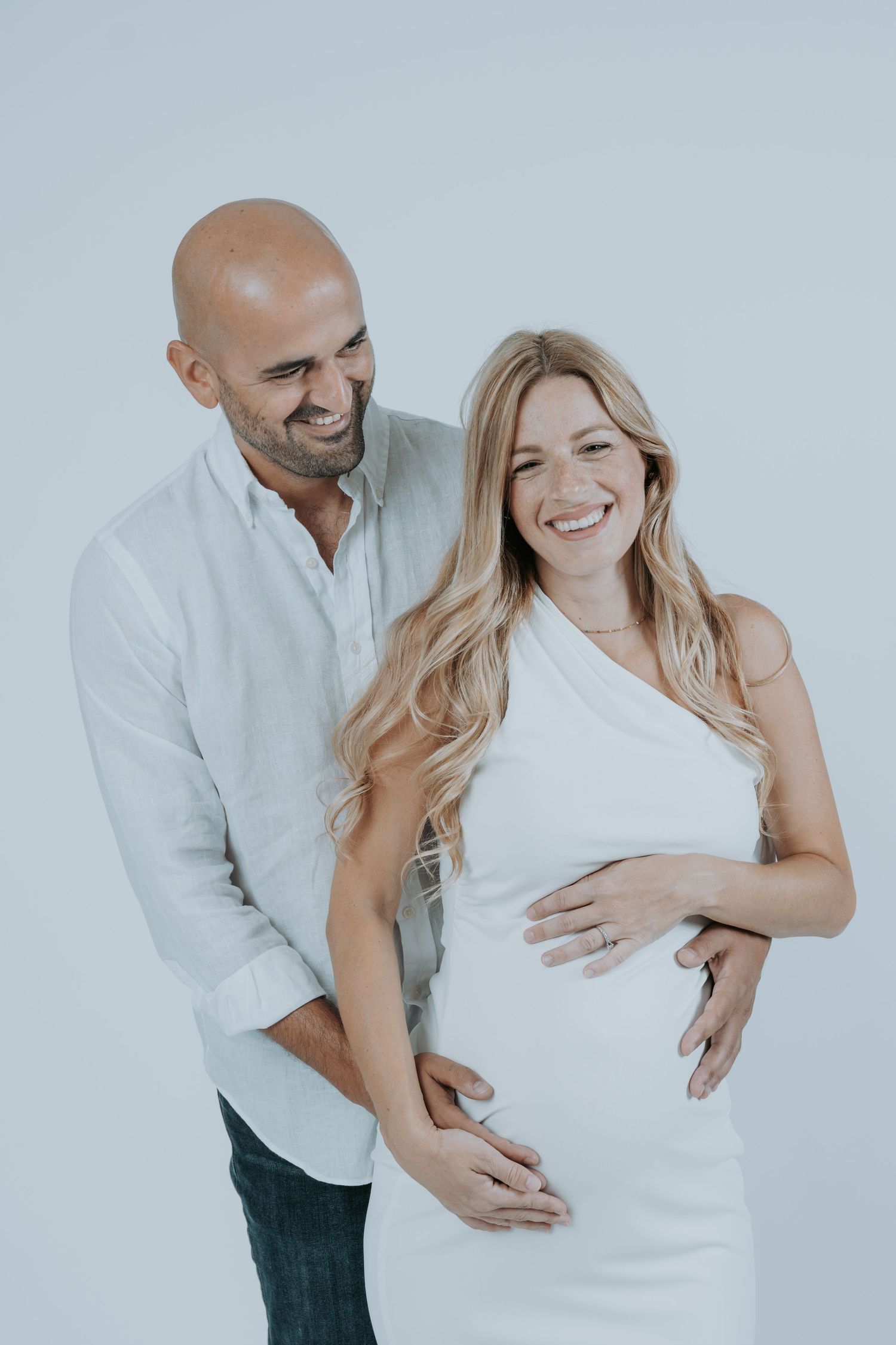 Couple in white outfits sharing intimate candid moments against light background.