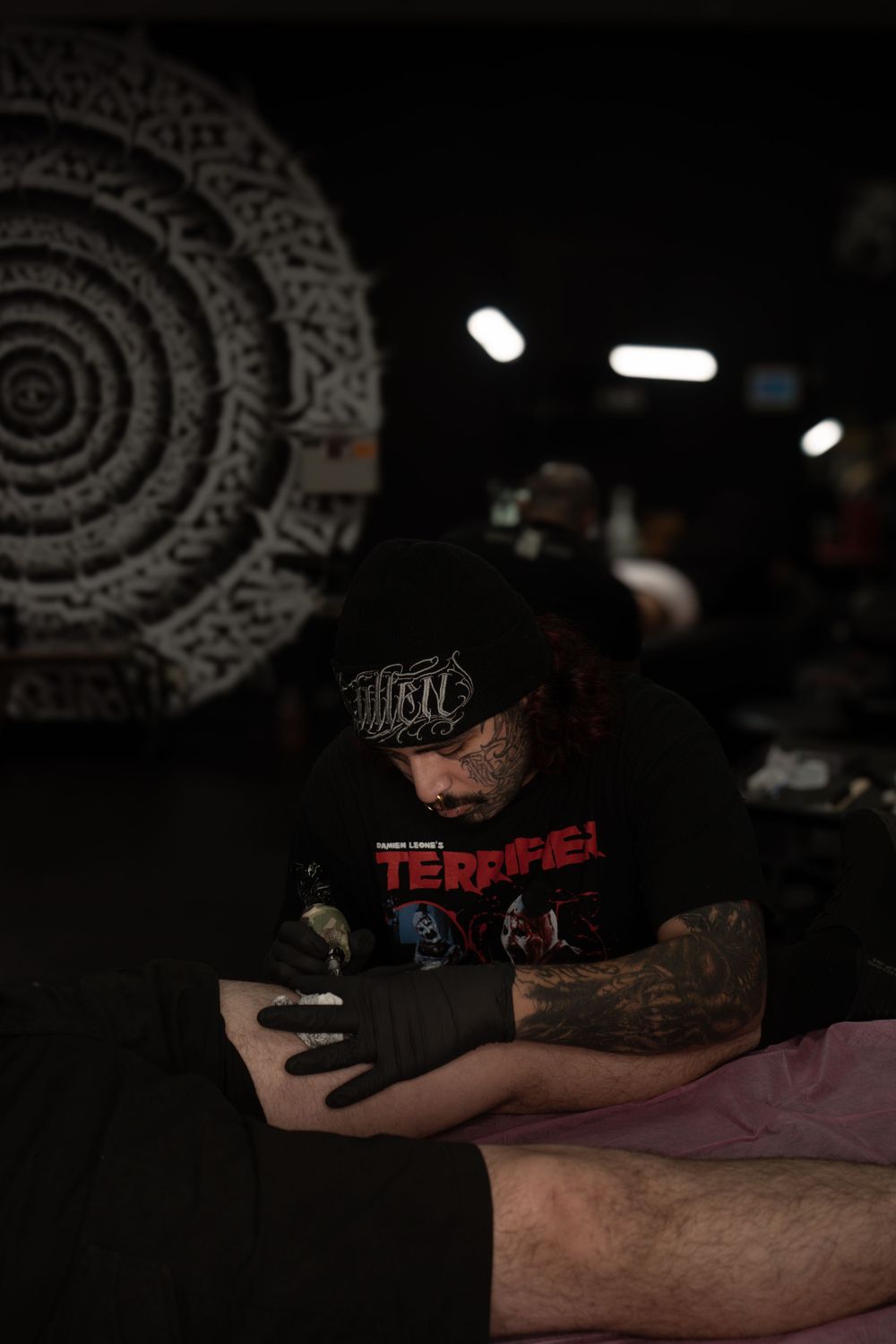 A series of dark, moody photos showing a tattoo artist working on a client's arm in a dimly lit studio with decorative wall art.