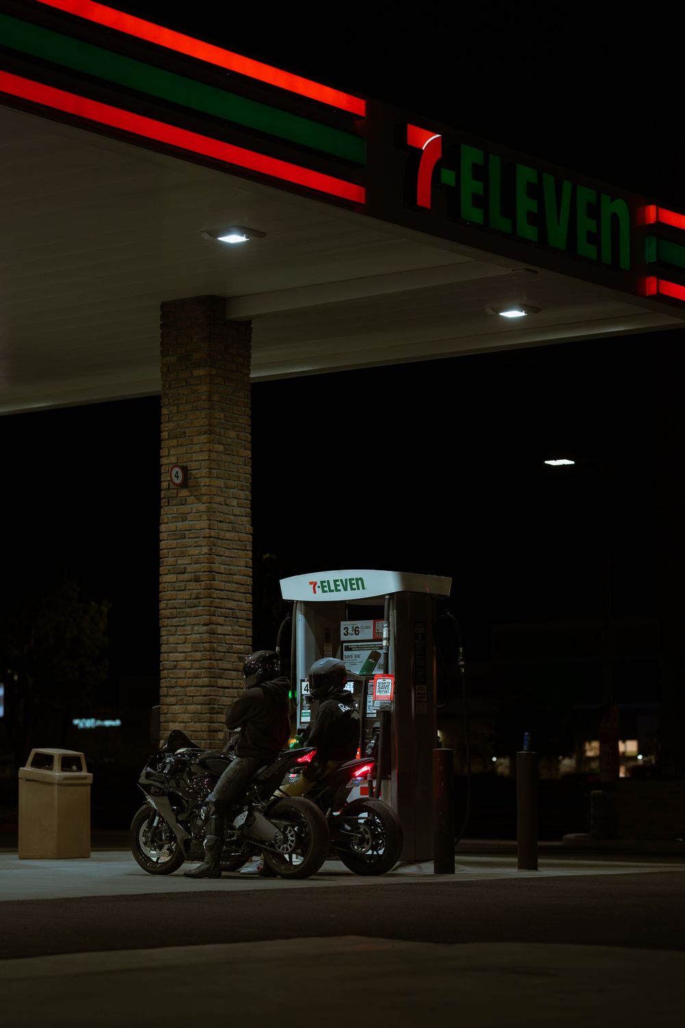 Motorcycles parked under illuminated 7-Eleven storefront at night with red neon lighting casting a glow.