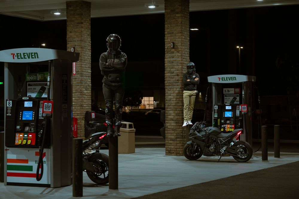 A dimly lit parking garage interior with motorcycles parked under brick columns and fluorescent lighting.