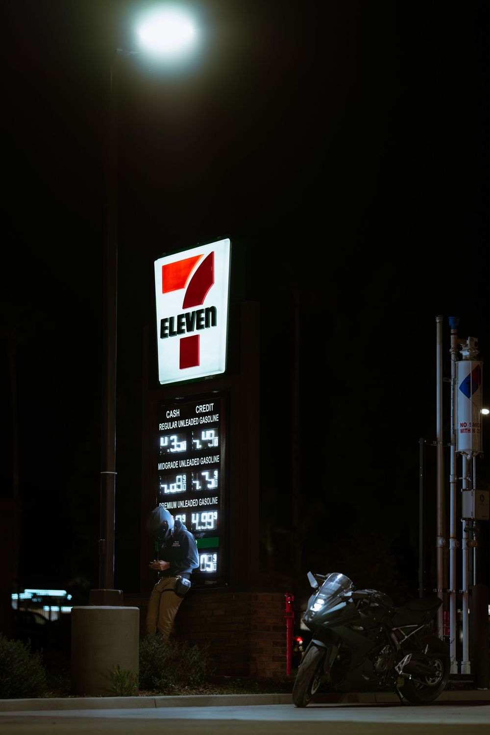 A dark gas station at night with illuminated red and white signage and a parked motorcycle visible.