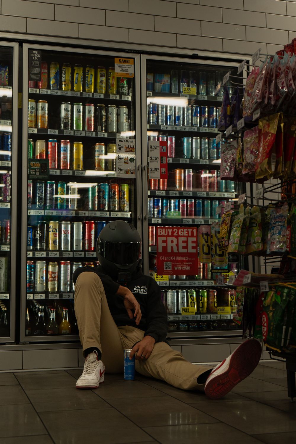 Convenience store interior with people lying on floor near refrigerated beverage cases at night.
