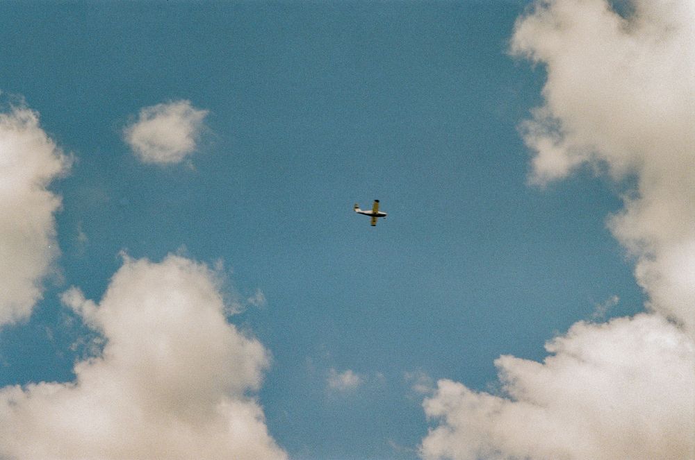 Small airplane silhouetted against blue sky with white fluffy clouds.