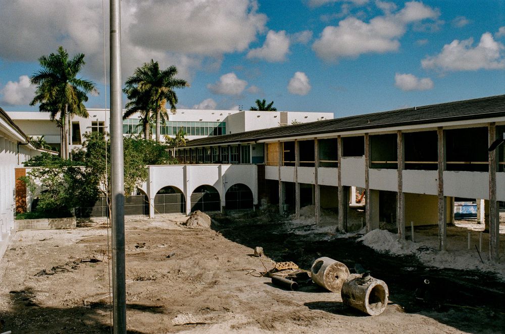 Abandoned tropical building with palm trees and construction debris in foreground.