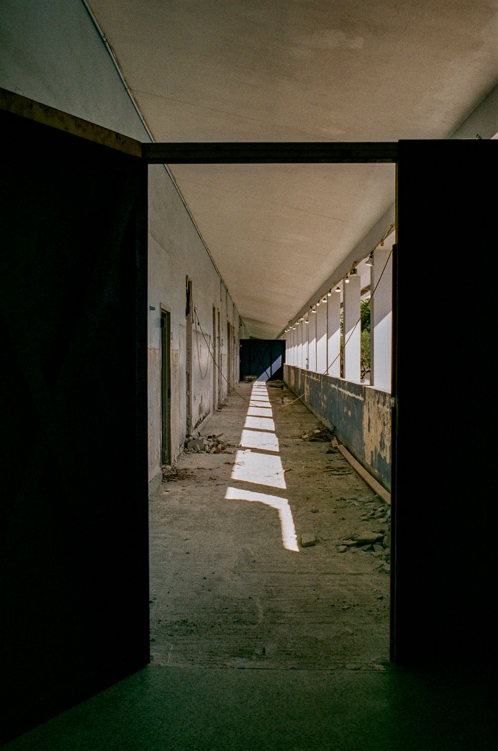 Sunlight streams through windows in an abandoned corridor creating dramatic shadows on the concrete floor.