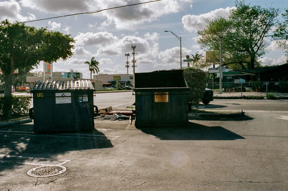 Two small utility sheds stand in an empty parking lot under cloudy skies.