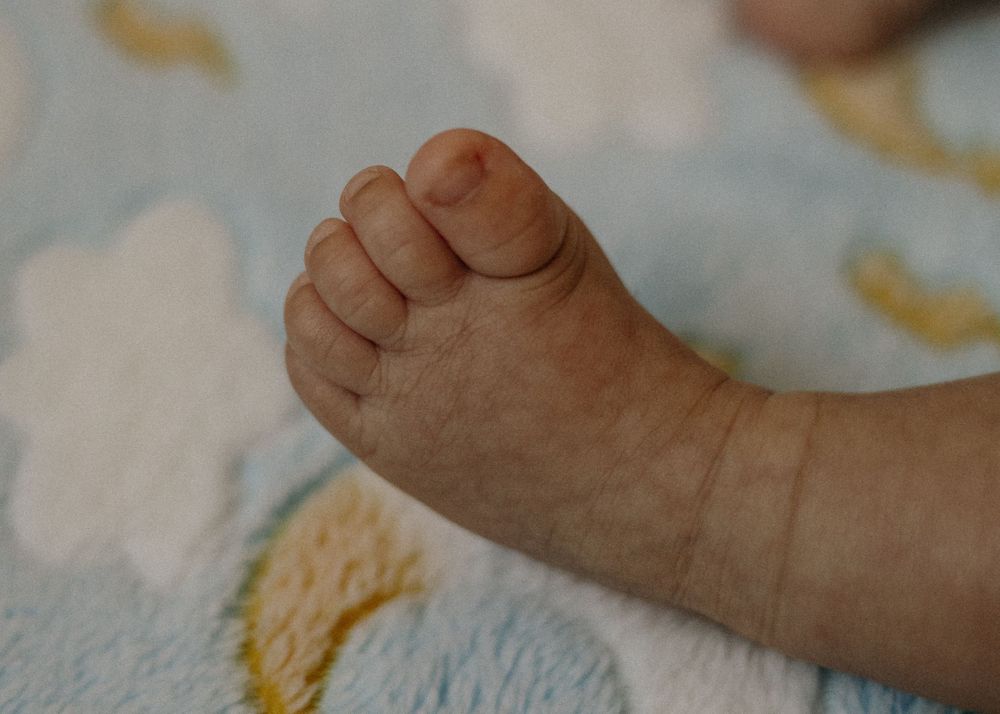 Close-up photograph of a tiny baby foot against a soft blue and yellow patterned blanket.