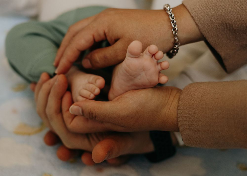 Gentle hands holding and caressing tiny baby feet in a tender close-up photo.