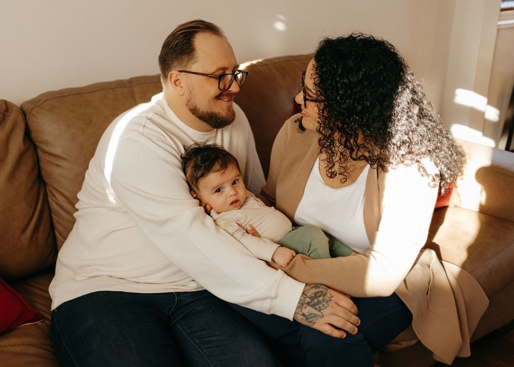A family relaxes on a brown leather couch together, sharing an intimate moment on a sunny afternoon.