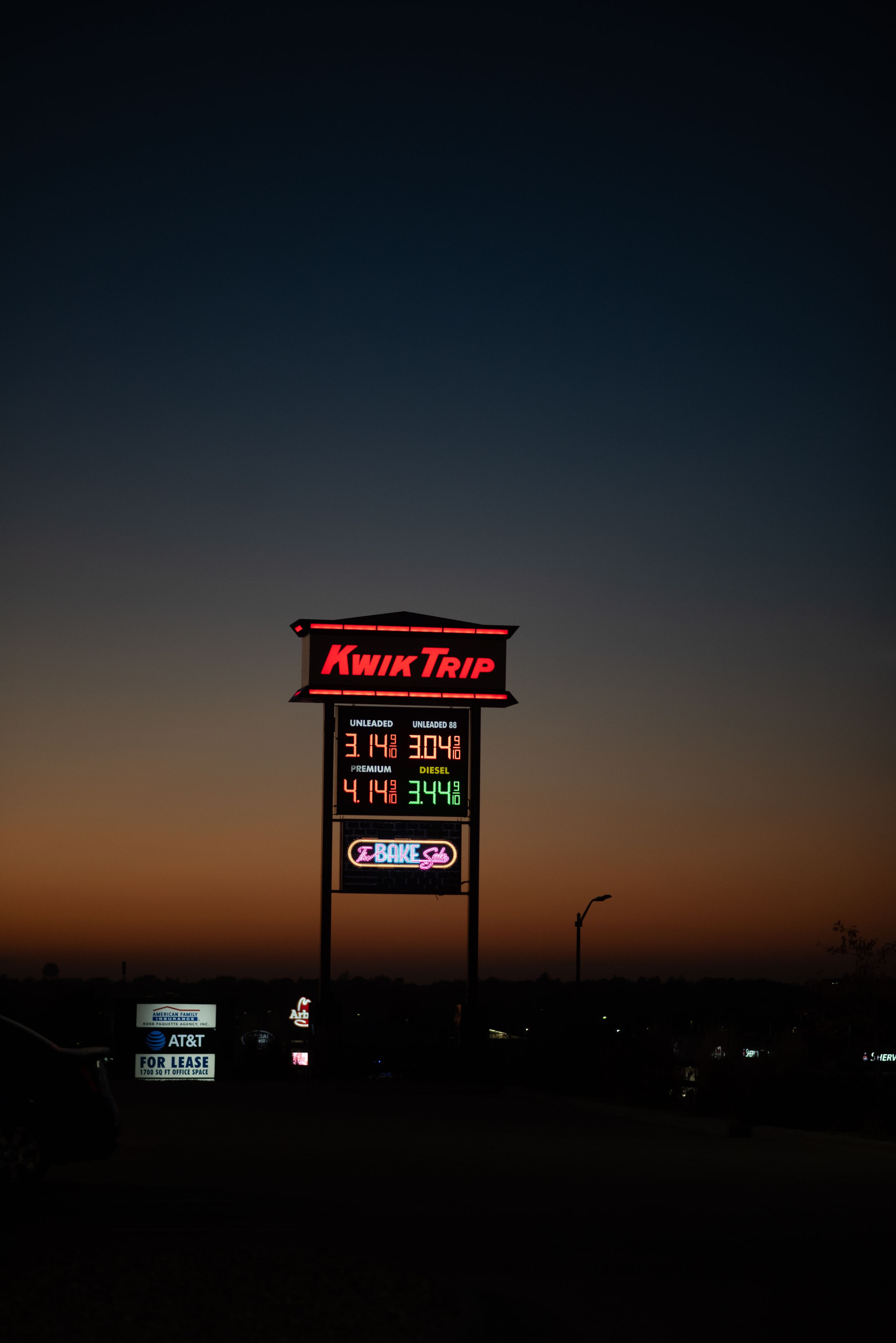 Illuminated Kwik Trip convenience store sign glows against a dark sunset sky with price displays visible.