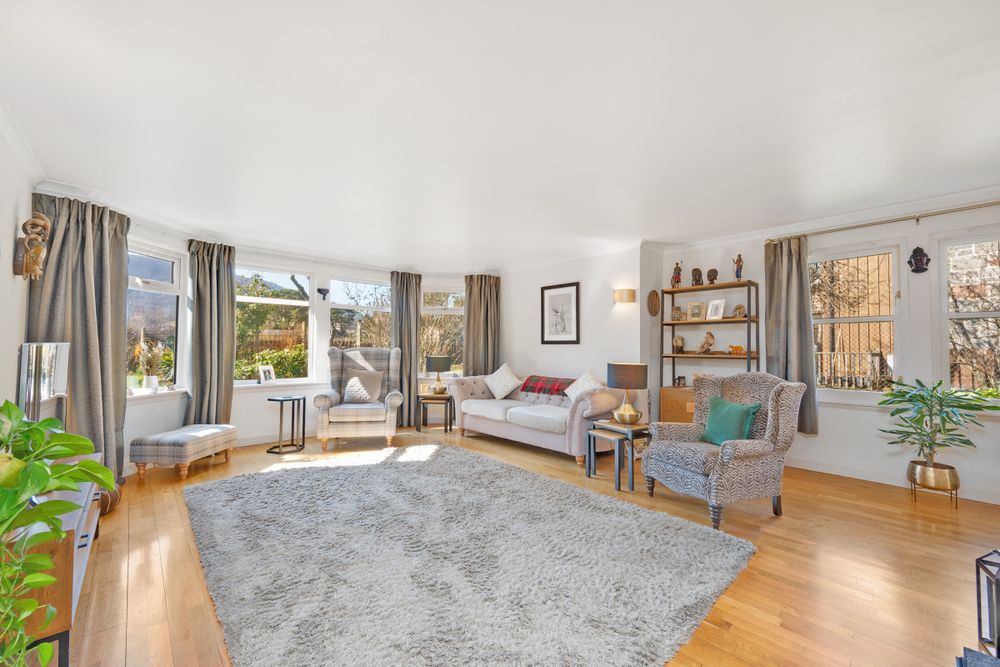 Bright living room with hardwood floors, gray rug, modern furniture, and large windows letting in natural light.