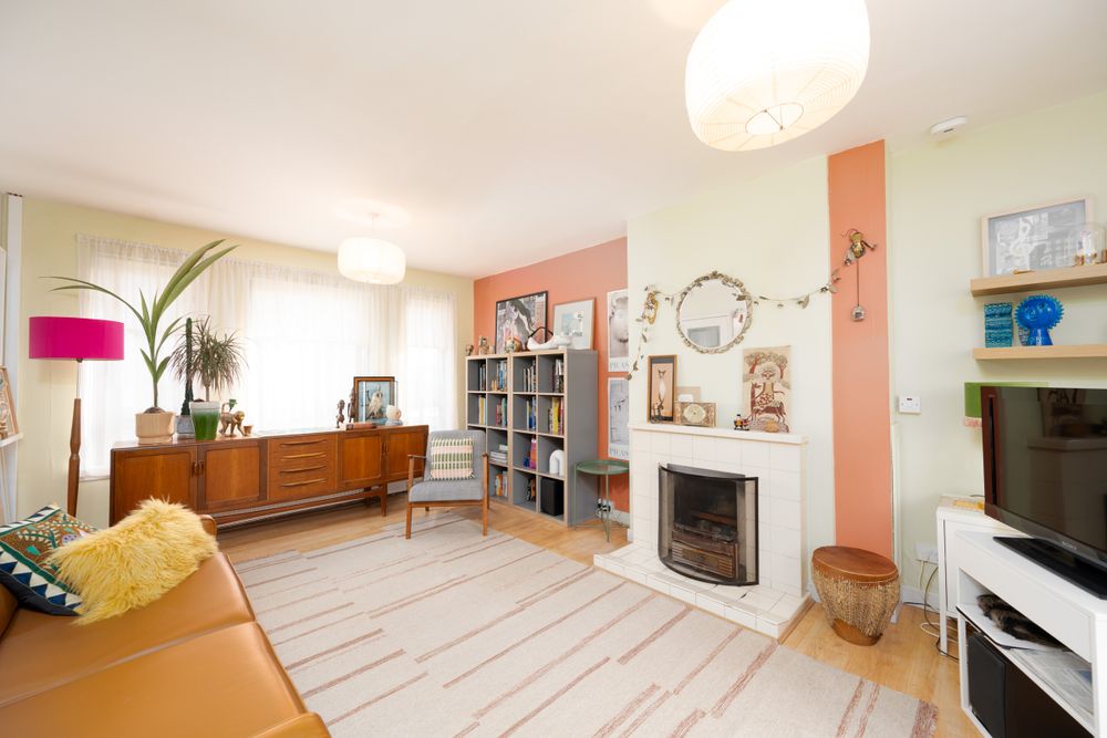 Bright modern living room with coral accent wall, white fireplace, mid-century furniture and grey striped area rug.
